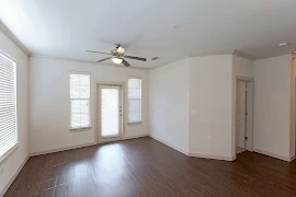 apartment living room with wood-inspired flooring, a patio door flanked by windows, a ceiling fan overhead, and a third window with blinds 