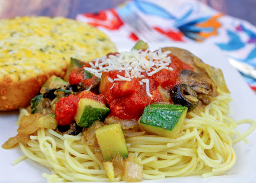 Angel hair pasta on a plate topped with sauteed vegetables.