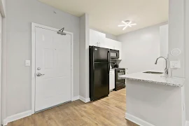 Apartment entry door open to a kitchen with white cabinets and a breakfast bar with stone countertop 