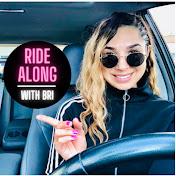 A female with round black sunglasses sits on the drivers side of the car, with steering wheel in front of her. She has long blonde hair and is pointing at a circle in the thumbnail which reads Ride Along With Bri.
