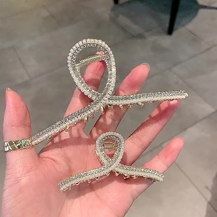 Presilha de cabelo cruz de metal com pérola e strass, um acessório elegante que adiciona brilho e sofisticação ao seu penteado.
