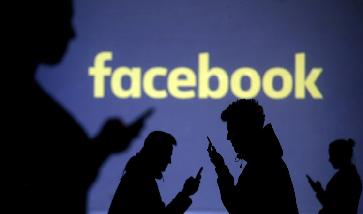 Silhouettes of mobile users are seen next to a screen projection of Facebook logo in this picture illustration taken March 28, 2018.