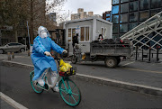 An epidemic control worker wears PPE as she passes workers as they prepare to remove a Covid-19 nucleic acid testing booth from a site in Chaoyang District on December 3, 2022 in Beijing, China. 