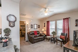 Alternate view of furnished living room with ceiling fan, two windows, and neutral colored carpet and walls