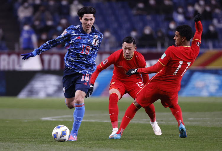 China's Xin Xu and Alan Carvalho (11) challenge Japan's Takumi Minamino during a World Cup qualifier at Saitama Stadium in Saitama, Japan