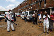 Members of the health services disinfect the Madala hostel in Alexandra, Johannesburg, as the South African government continues efforts to control the outbreak of Covid-19. Residents stand in line to receive disinfectant.