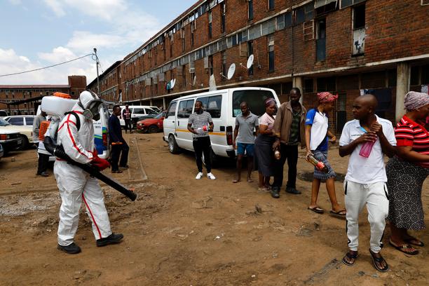 Members of the health services disinfect the Madala hostel in Alexandra, Johannesburg, as the South African government continues efforts to control the outbreak of Covid-19. Residents stand in line to receive disinfectant.