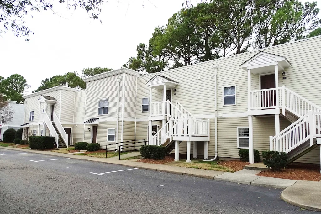 Dundale Square apartment building with light siding, white stairs, and a sidewalk and parking in front.