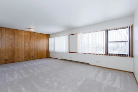 Living room with wood paneled accent wall, wall of windows, and carpeted flooring