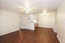 Living room facing kitchen and dining area with ceiling fan, wood inspired floors, and neutral colored walls