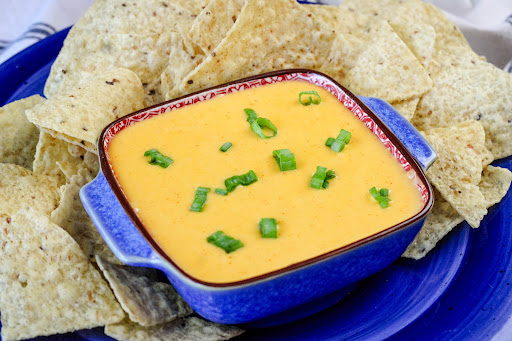 A bowl of Sriracha Queso Dip with scallions sprinkled on top.