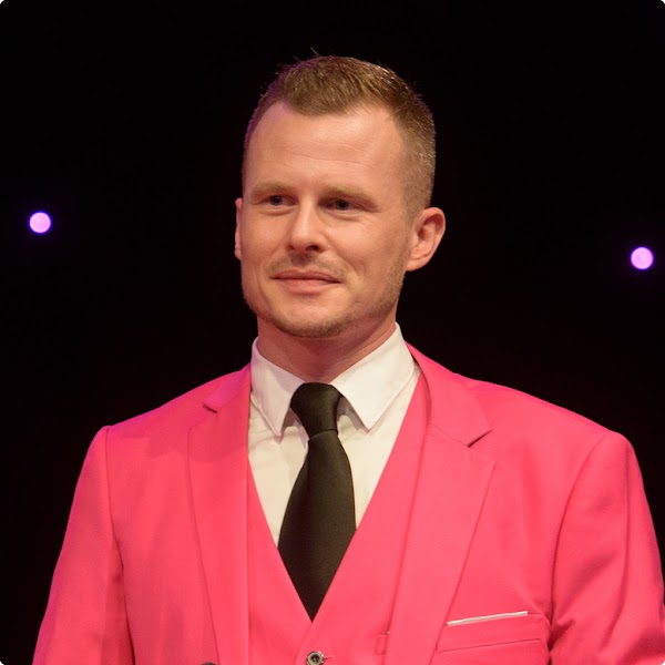 Adrian Knecht, Co-presidente di Pink Cross, indossa un abito color fuchsia, in piedi su un palcoscenico.