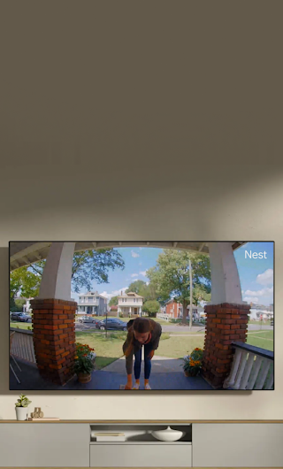 Un écran de télévision installé dans un salon montrant un livreur sur le perron qui fait signe à la sonnette vidéo.