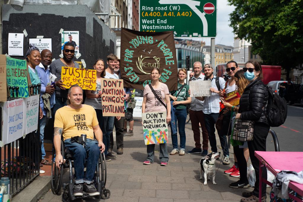 Black and white activists and one in a wheelchair with placaards outside Congolese embassy