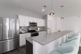 Kitchen with breakfast bar, gray stone countertops, white cabinets, tile backsplash, tall ceilings, and stainless appliances