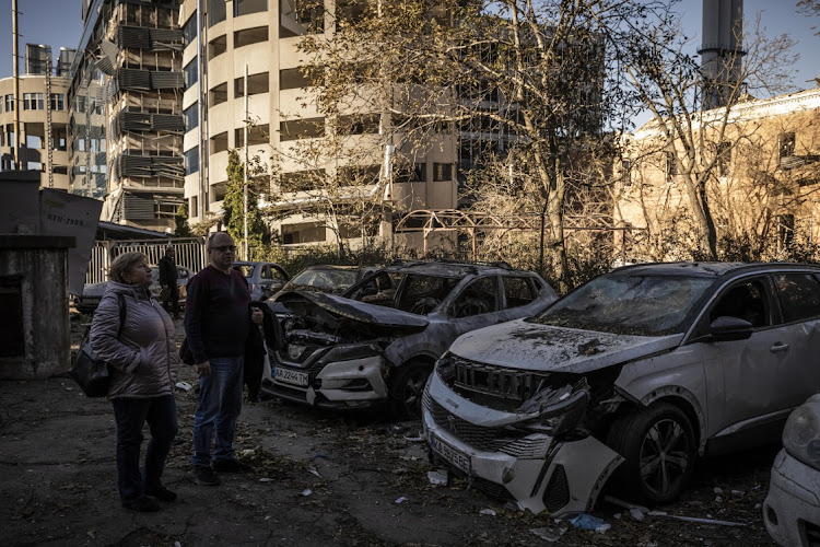 People look at their destroyed cars that stand amid damage caused by a missile strike in a residential area near Tower 101 not far from Kyiv's main train station on October 11, 2022 in Kyiv, Ukraine.