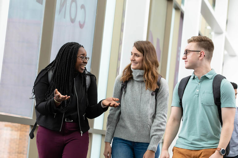 Three students talk while walking in the skyway.