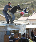 A Nelson Mandela Bay metro police officer grabs a man as he throws his child off the roof of a shack at the Joe Slovo informal settlement in Port Elizabeth on April 12 2018.