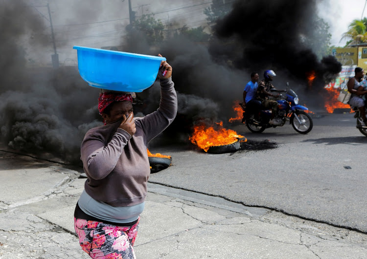 A woman covers her nose while walking past a burning road block as anger mounted over fuel shortages that have intensified as a result of gang violence, in Port-au-Prince, Haiti, July 13, 2022.
