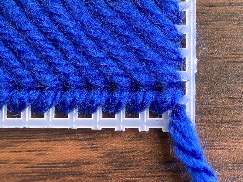 making a whip stitch on plastic canvas using blue colored yarn