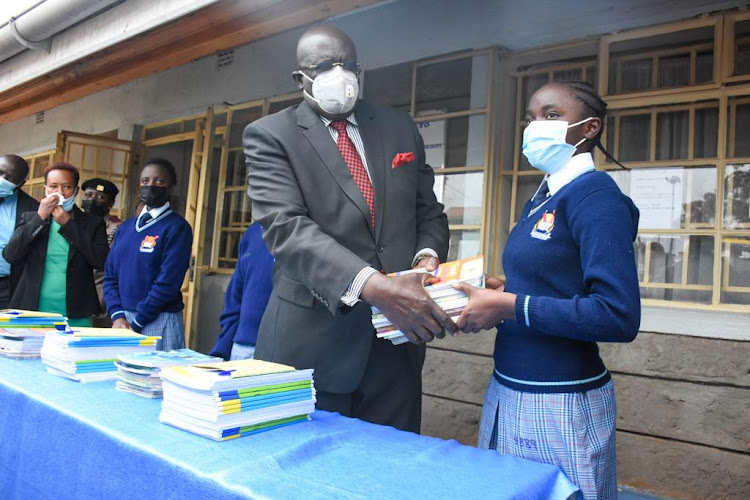 Education CS George Magoha hands over Form 1 textbooks to Bianca Nyambura during a mop up exercise to ensure all Form 1 students report to school on September 1.