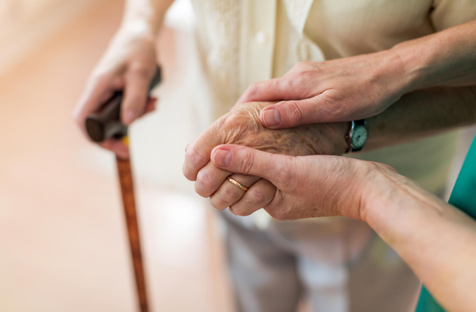 A close of photo of hands. a young person hold the hand of a senior. the senior has a cane in the opposite hand.