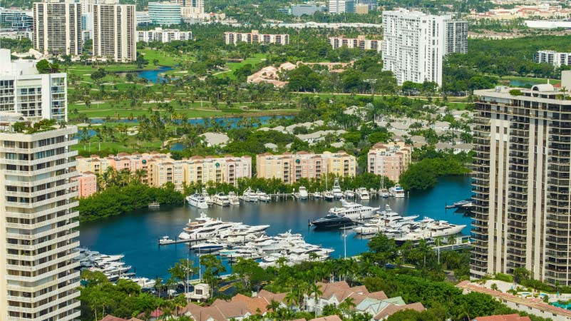 Aerial view of Aventura Marina and high-rise condos with a golf course in the background in Aventura, Florida.