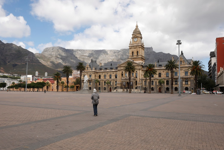 A clock shows the time at noon, as a man walks near Cape Town's city hall, during the novel coronavirus outbreak, in Cape Town on March 31 2020. REUTERS/MIKE HUTCHINGS