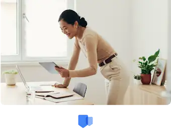 A woman leaning over her desk looking over her accolades and rewards on her tablet.