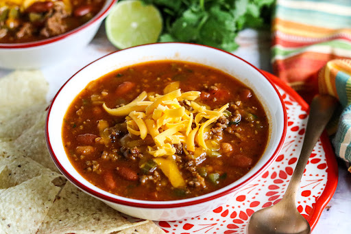 A bowl of Kimmy's Zesty Chili with shredded cheddar cheese on top.