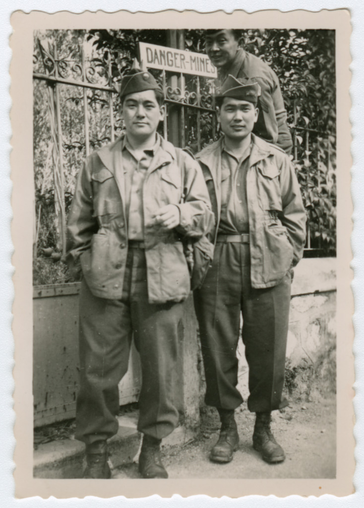 Three Nisei soldiers posing in front of a sign that reads "Danger - Mines."