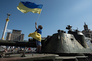A boy holds a Ukrainian national flag as he stands on top of captured Russian military vehicles. Picture: GETTY IMAGES/ALEXEY FURMAN