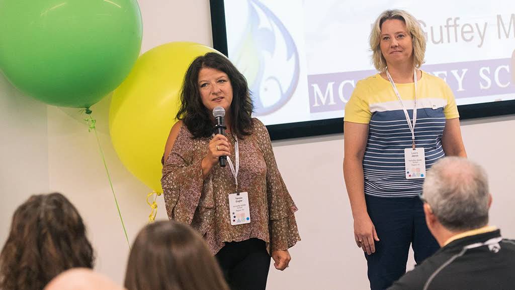 Two women explain a topic, one of them speaks holding a microphone in her right hand