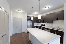 Apartment entry door open to the kitchen with an island, wood-inspired flooring, and pendant lighting overhead 