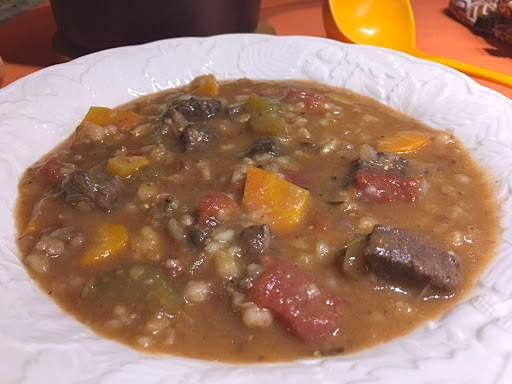 Barley soup in a white bowl with a yellow ladle in the background.