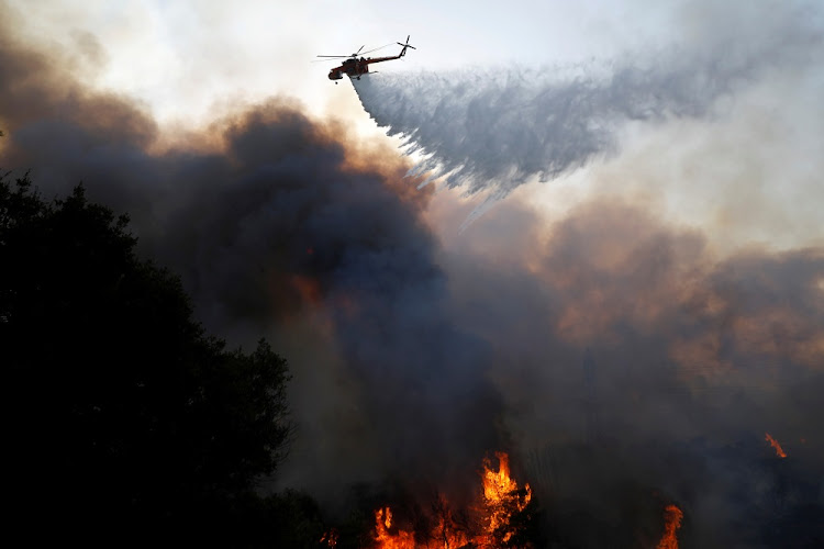 A firefighting helicopter makes a water drop as a wildfire burns at Varympompi suburb north of Athens, Greece, August 3 2021.