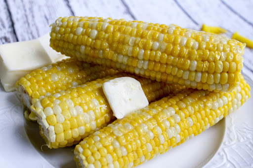 Ears of corn on a plate with a pat of butter.