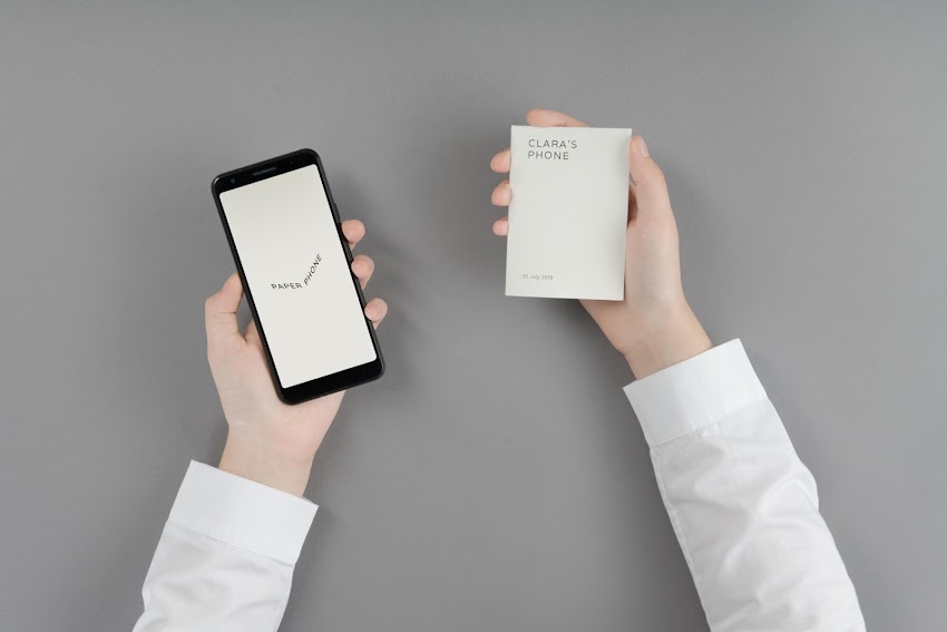 White hands hold a tablet and a notebook against a grey background.