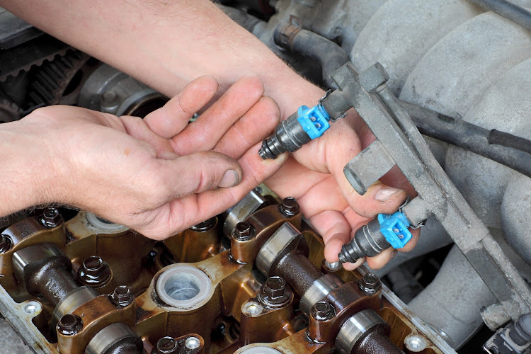 A mechanic inspects a fuel injector on a petrol engine.