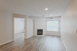 Living room with wood-inspired flooring, fireplace in the corner, window with blinds, light walls and white trim