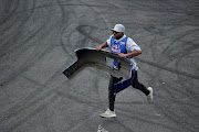 A man runs with a car bumper that fell off a car's competitor. 