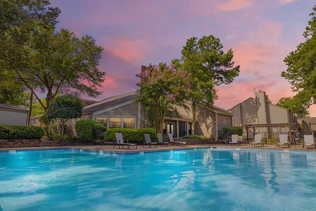 The Residence at Village Green Apartments pool with lounge chairs surrounding and view of apartment buildings at dusk