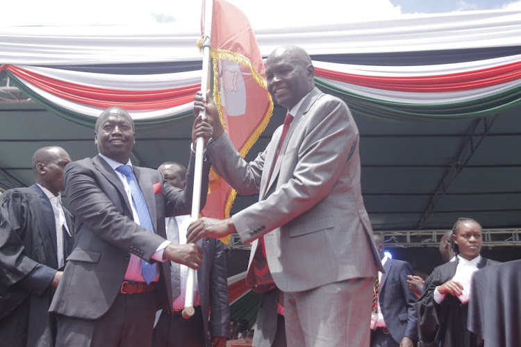 Outgoing Baringo Governor Stanley Kiptis(right) hands over flag to Governor-elect Benjamin Cheboi during his swearing in ceremony at Kabarnet showground on Thursday.