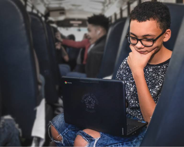 En elev med briller som sitter på bussen til skolen og ser konsentrert på en Chromebook-enhet