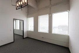 Living room with three curved windows, hanging modern light fixture, white walls, and dark gray carpet