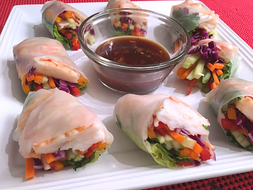 Rolls stuffed with shrimp and vegetables on a white plate with dipping sauce in the middle.