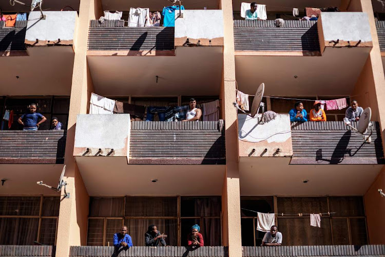 BOXED IN: Residents on coronavirus lockdown in a block in Hillbrow, Johannesburg, look on as police patrol the streets on Saturday