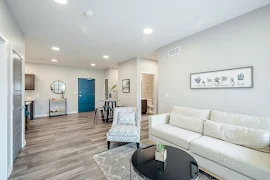 Furnished living room, with view of dining area, wood plank floors, gray walls, white trim, and recessed lighting