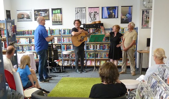 Bibliotheksleiterin Marion Meier-Esser im angeregten Gespräch mit Werner Burkard und dem Musiker Michael Lembach mit Gitarre.