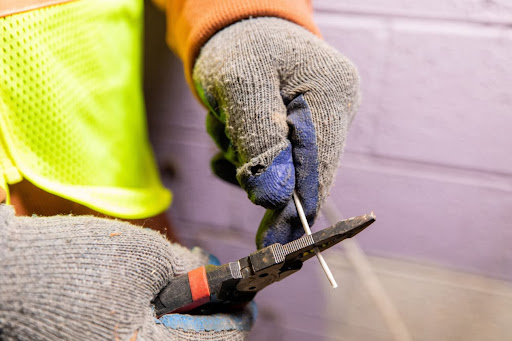 Image de mains dans des gants pour électricien tenant une pince et un fil